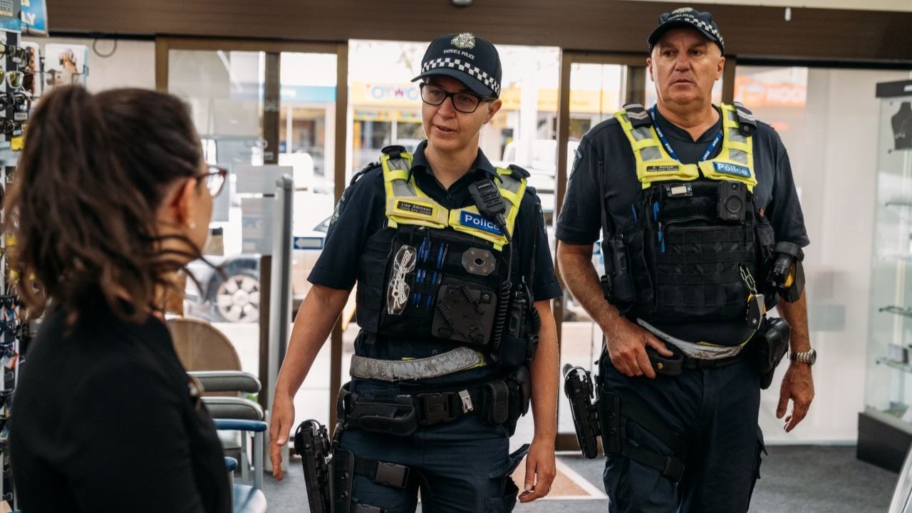 Two officers in police uniform walking into a store and speaking to a staff member. 